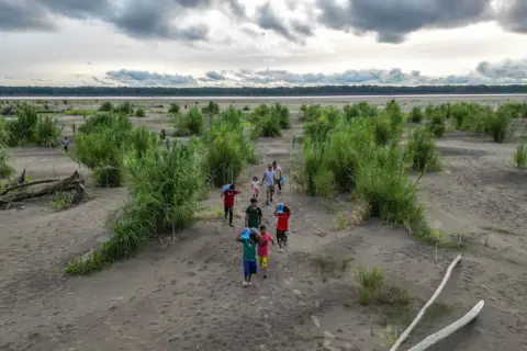 Luis Acosta/AFP Aerial view of Yagua Indigenous people carrying water and other goods due to the low level of the Amazon River at Isla de los Micos, Amazonas department, Colombia, on October 4, 2024. 